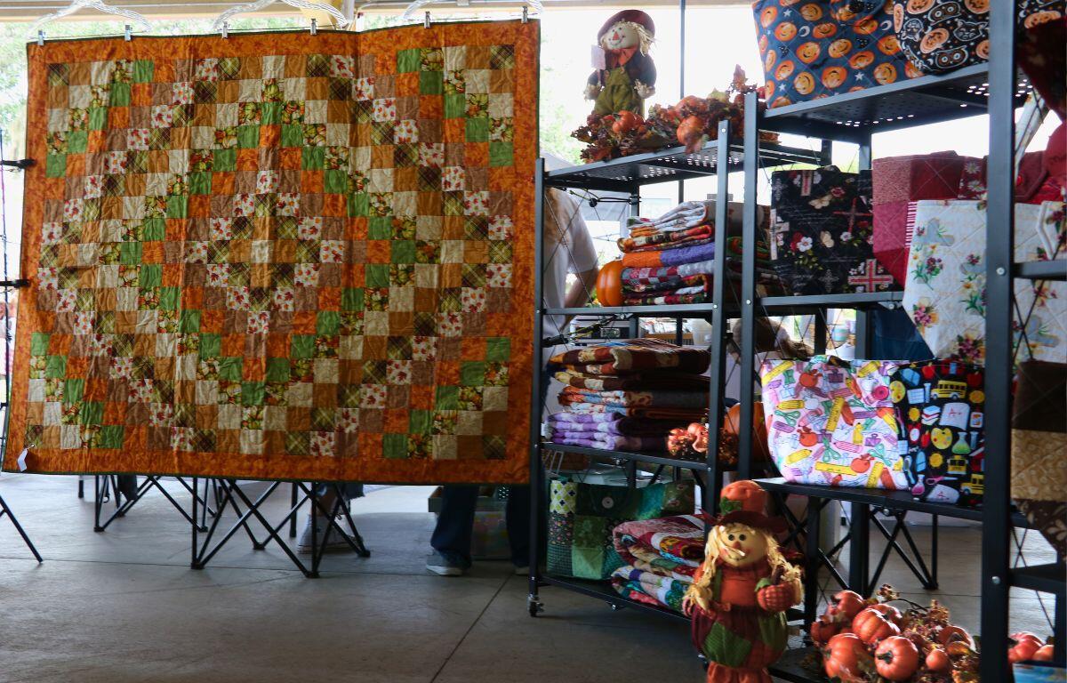 Fall colored quilts, bags and decor are set on shelves with one large quilt being strung up.