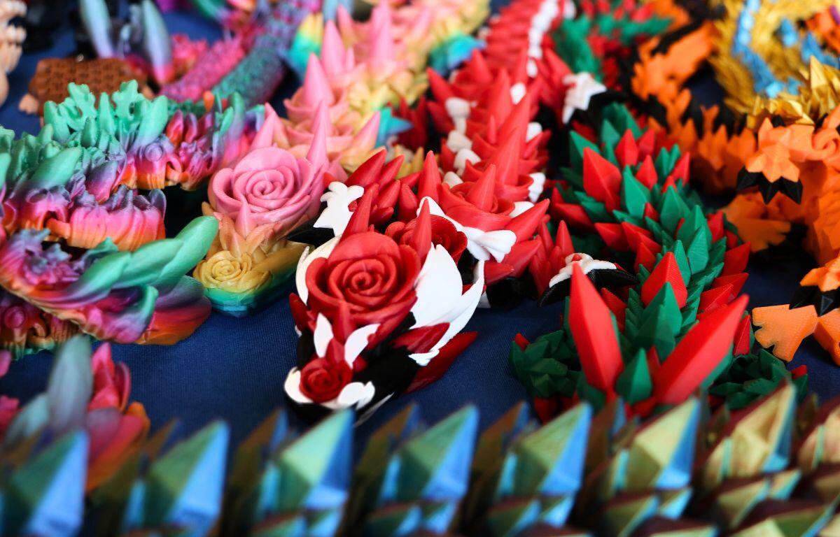 3D printed dragons with different colors line a table with a blue tablecloth.