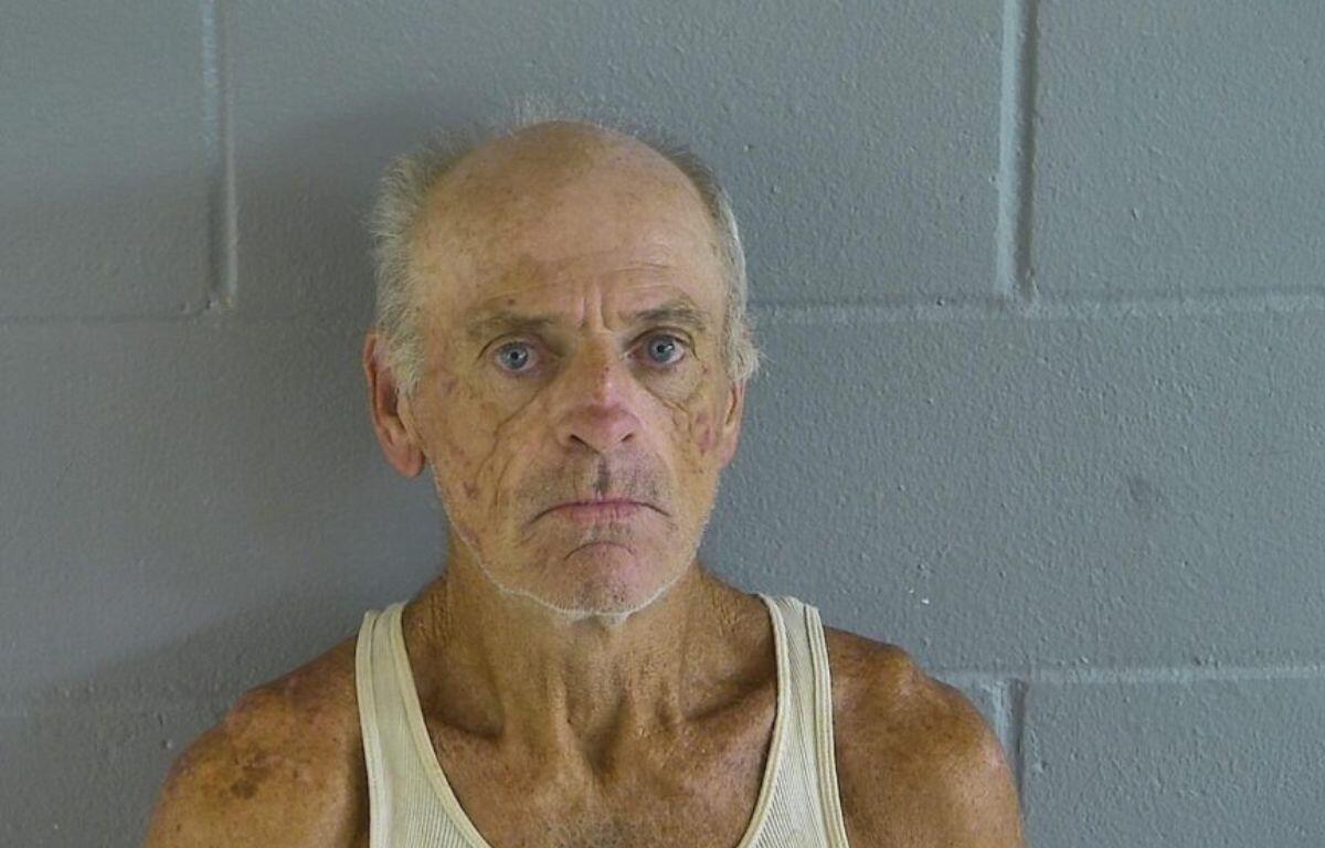 A man in an undershirt against a gray wall.