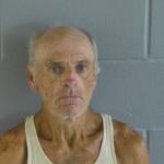 A man in an undershirt against a gray wall.