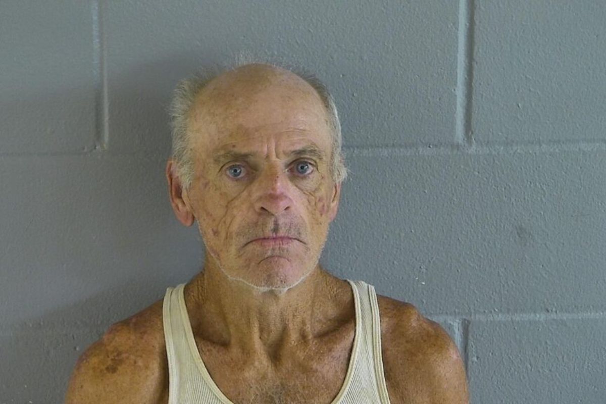 A man in an undershirt against a gray wall.