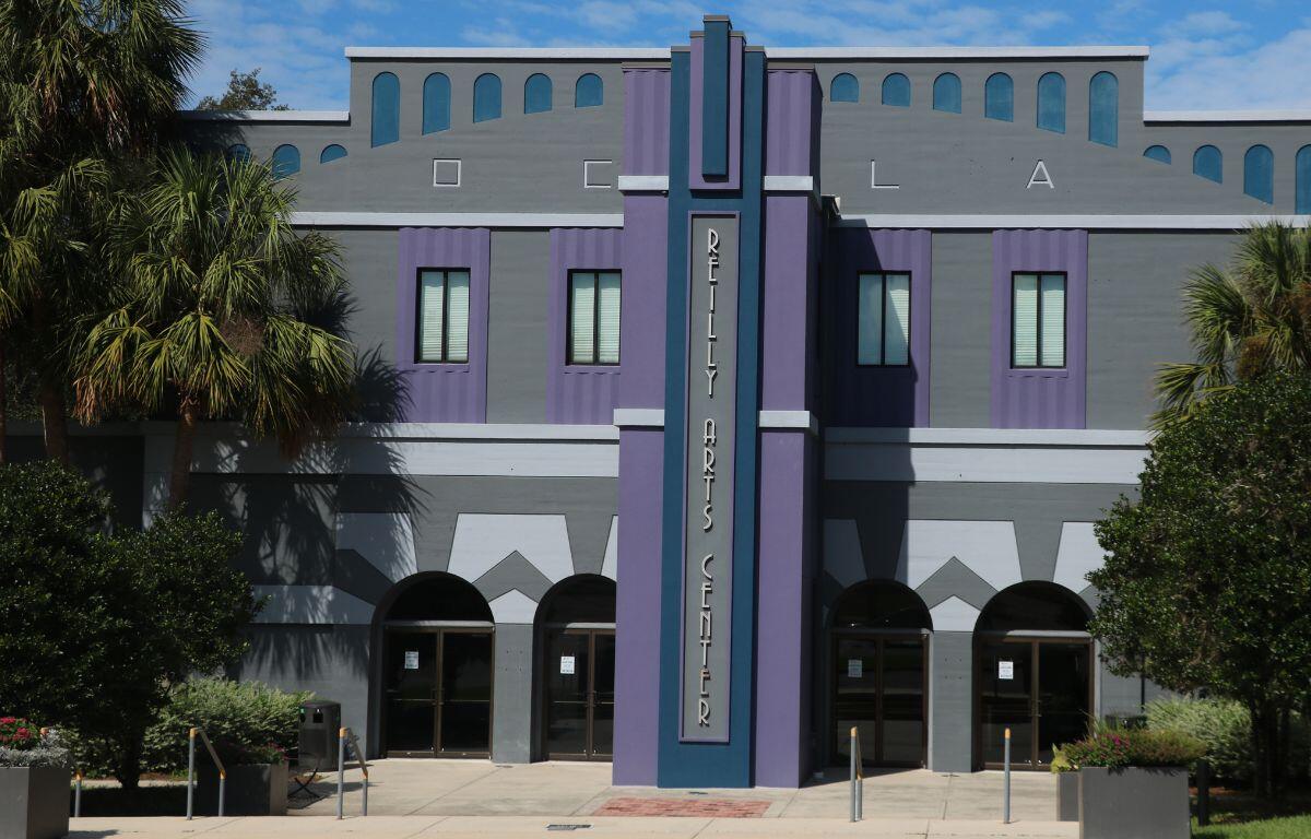 Front view of the Reilly Arts Center, featuring a gray and purple art deco facade with arched doorways and palm trees.