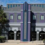 Front view of the Reilly Arts Center, featuring a gray and purple art deco facade with arched doorways and palm trees.