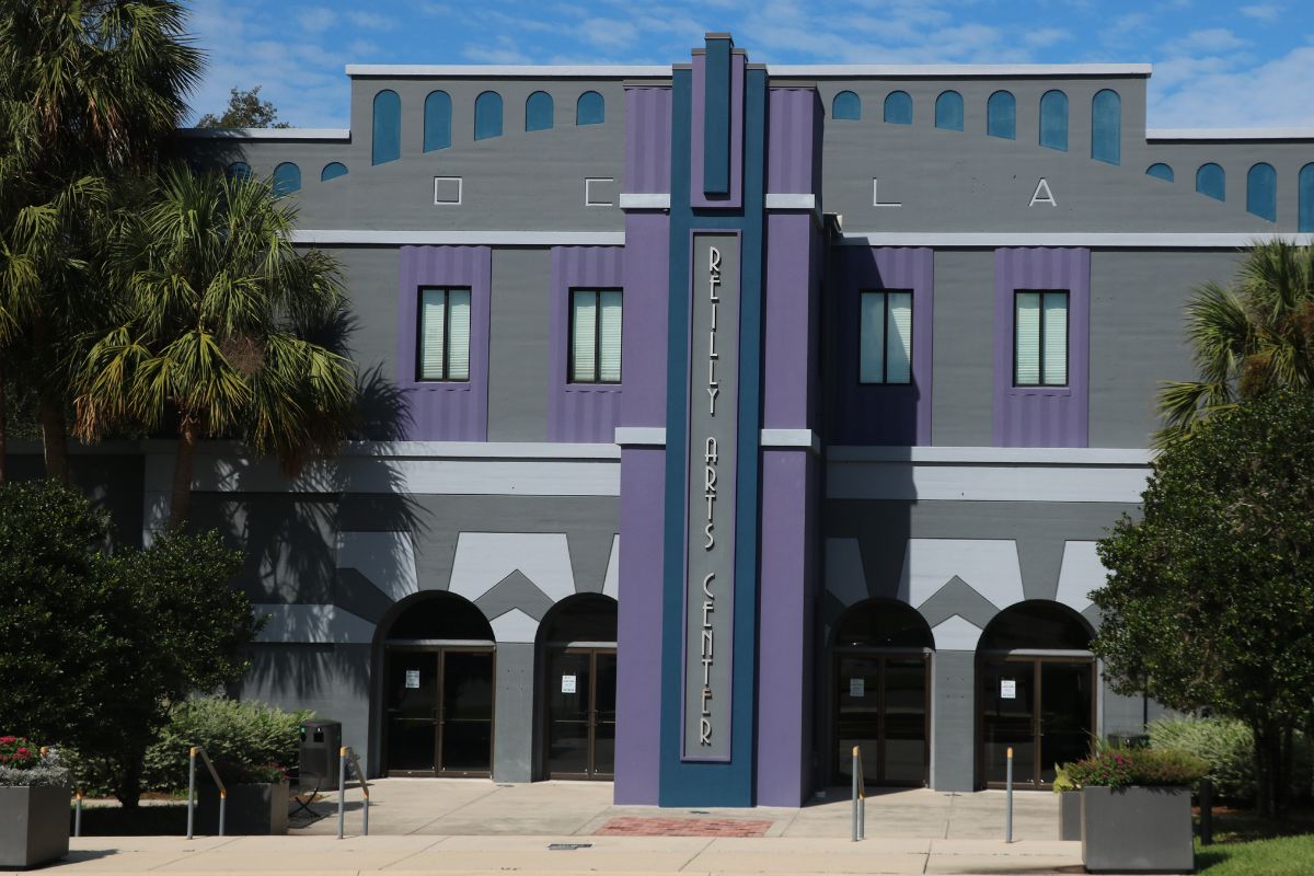 Front view of the Reilly Arts Center, featuring a gray and purple art deco facade with arched doorways and palm trees.