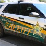 A front angle of a car with a green, yellow and white wrap with a monochrome American Flag on the back window sits next to a sidewalk. On the car reads, "Marion County Sheriff. Integrity. Honesty. Trust."