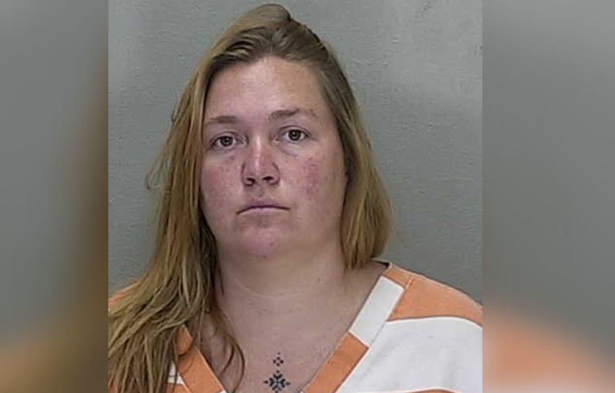 A woman in a white and orange jump suit standing against a gray wall.