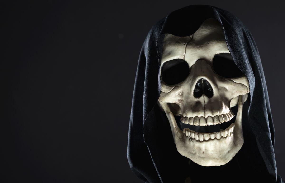 A cloaked skull peeking out of the shadows against a dark background.