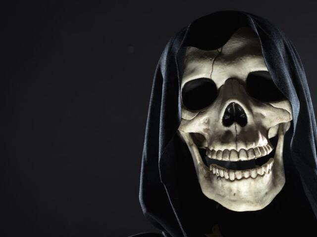 A cloaked skull peeking out of the shadows against a dark background.