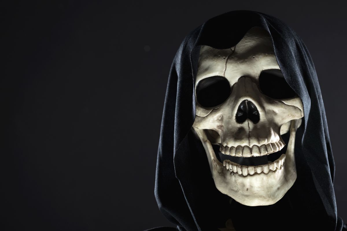 A cloaked skull peeking out of the shadows against a dark background.