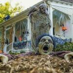 A zombie yard decoration in the foreground while a house decorated for Halloween with cobwebs and pumpkins sit behind it.