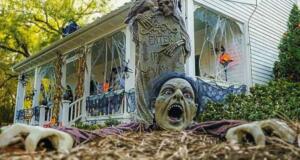 A zombie yard decoration in the foreground while a house decorated for Halloween with cobwebs and pumpkins sit behind it.