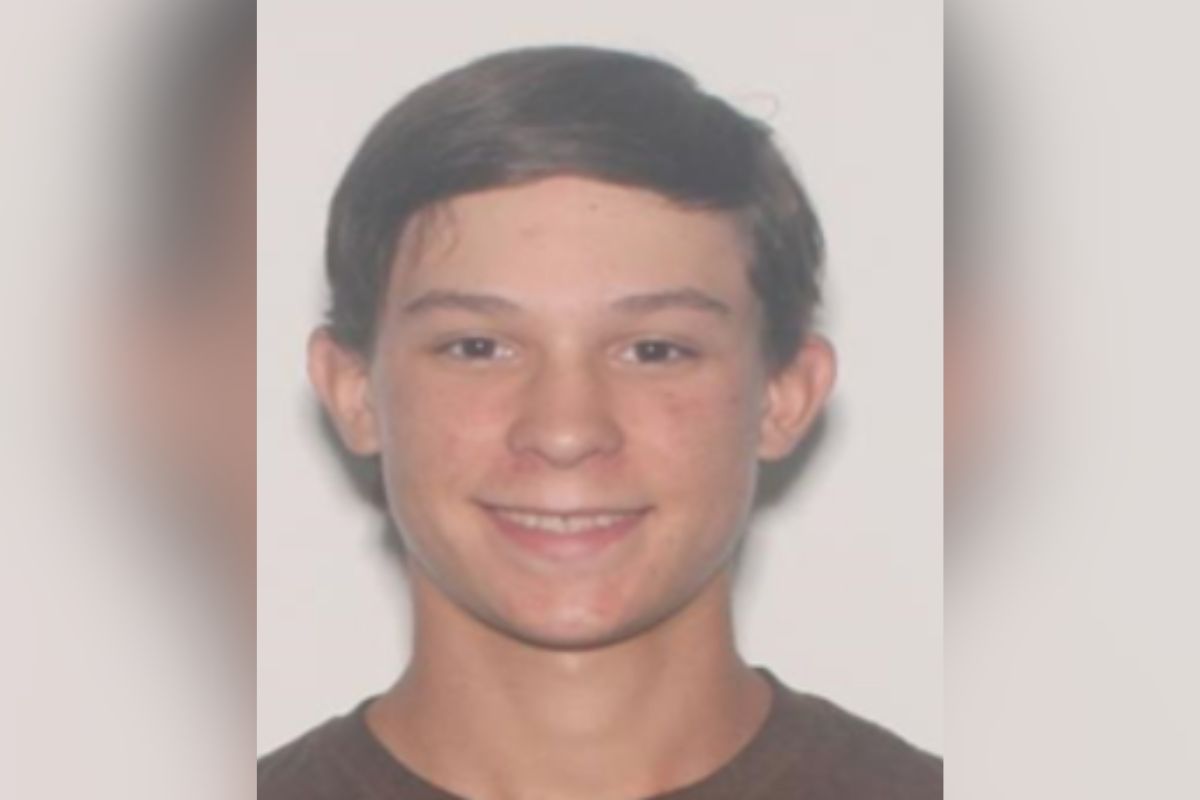 Headshot of 17-year-old Caden Speight, smiling, with short brown hair, wearing a dark shirt, against a plain light background.