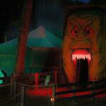 A large alien head facade stands tall in front of a building with an open mouth for guests to walk through. There are canopies in the background with writing on a wall reading, "Homestead Haunt."