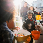 Two happy children in costumes Trick or Treating with their parents.