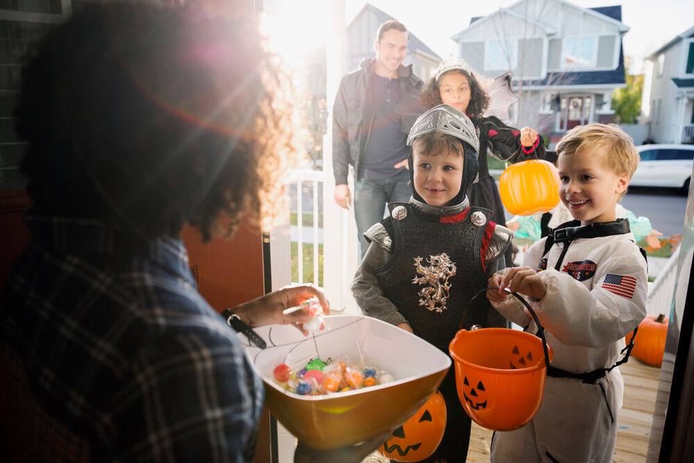 Two happy children in costumes Trick or Treating with their parents.