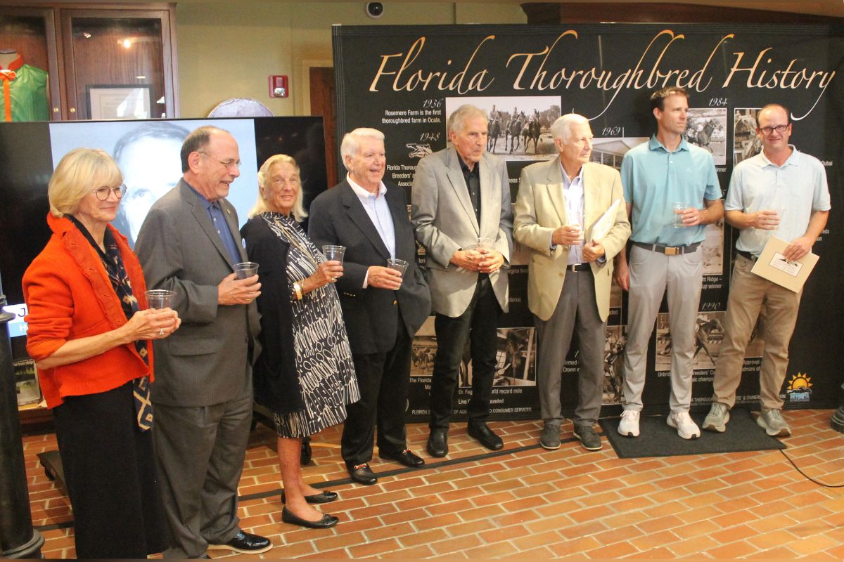A group of people standing in front of an exhibit placard, with a faux brick floor in the foreground.