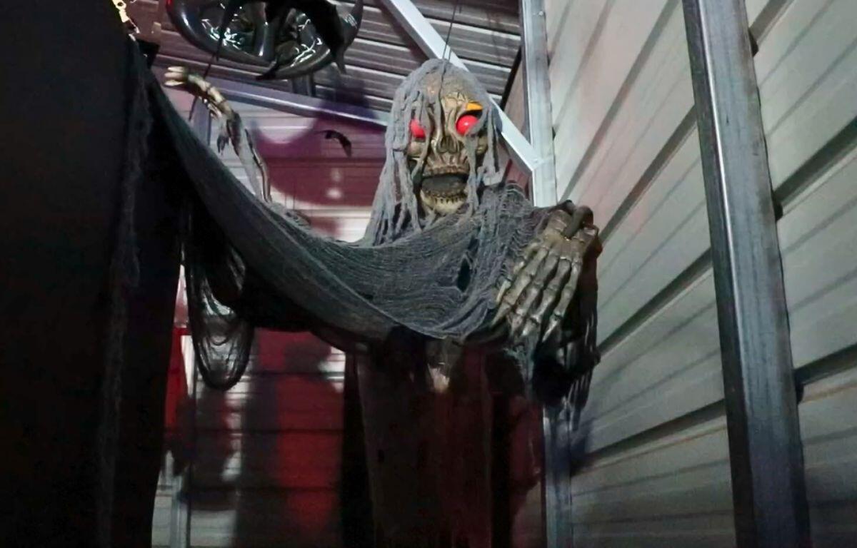 A ghostly skeleton with red eyes hangs from a ceiling with disheveled clothing. In the background is a warehouse setting.