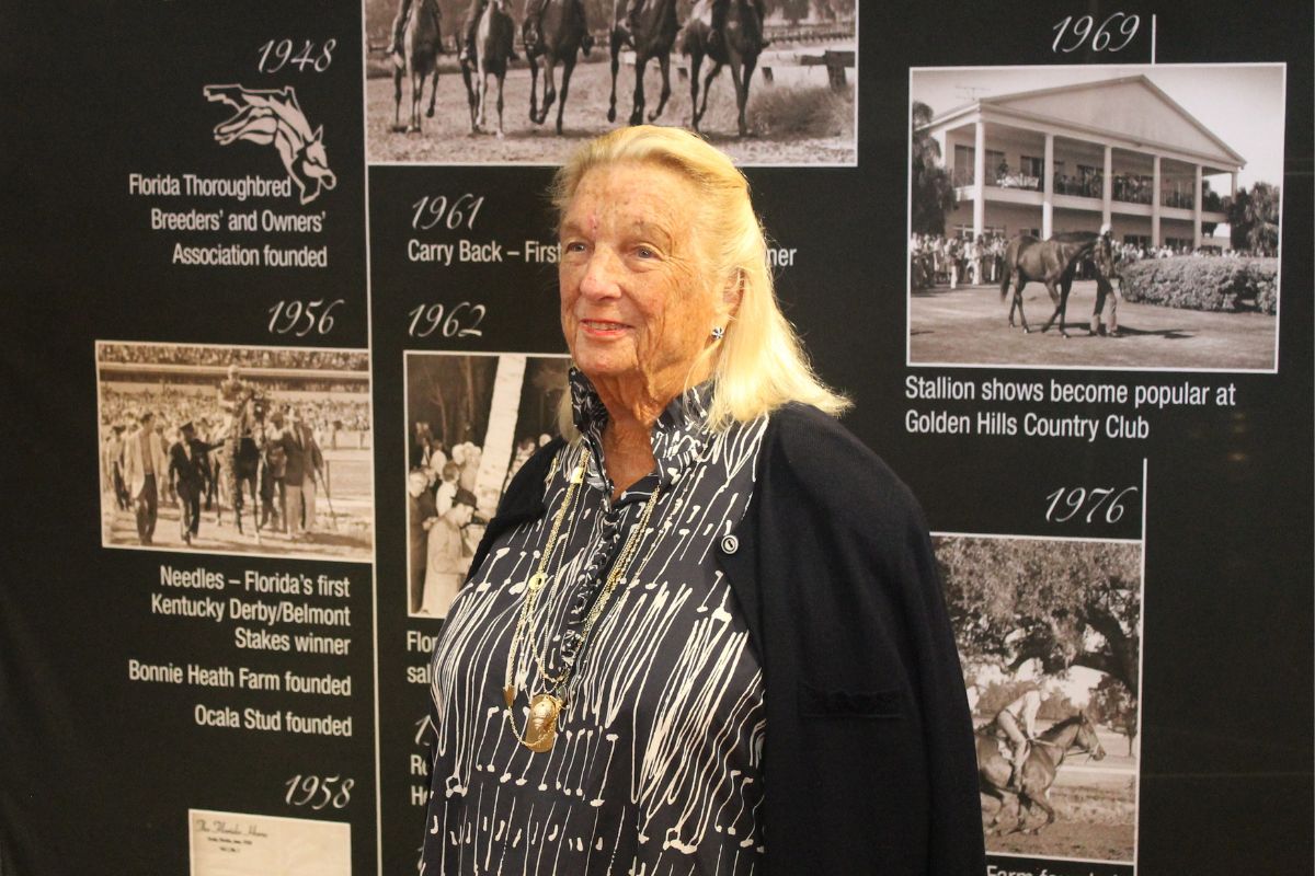 A well-dressed woman standing in front of an exhibit placard.