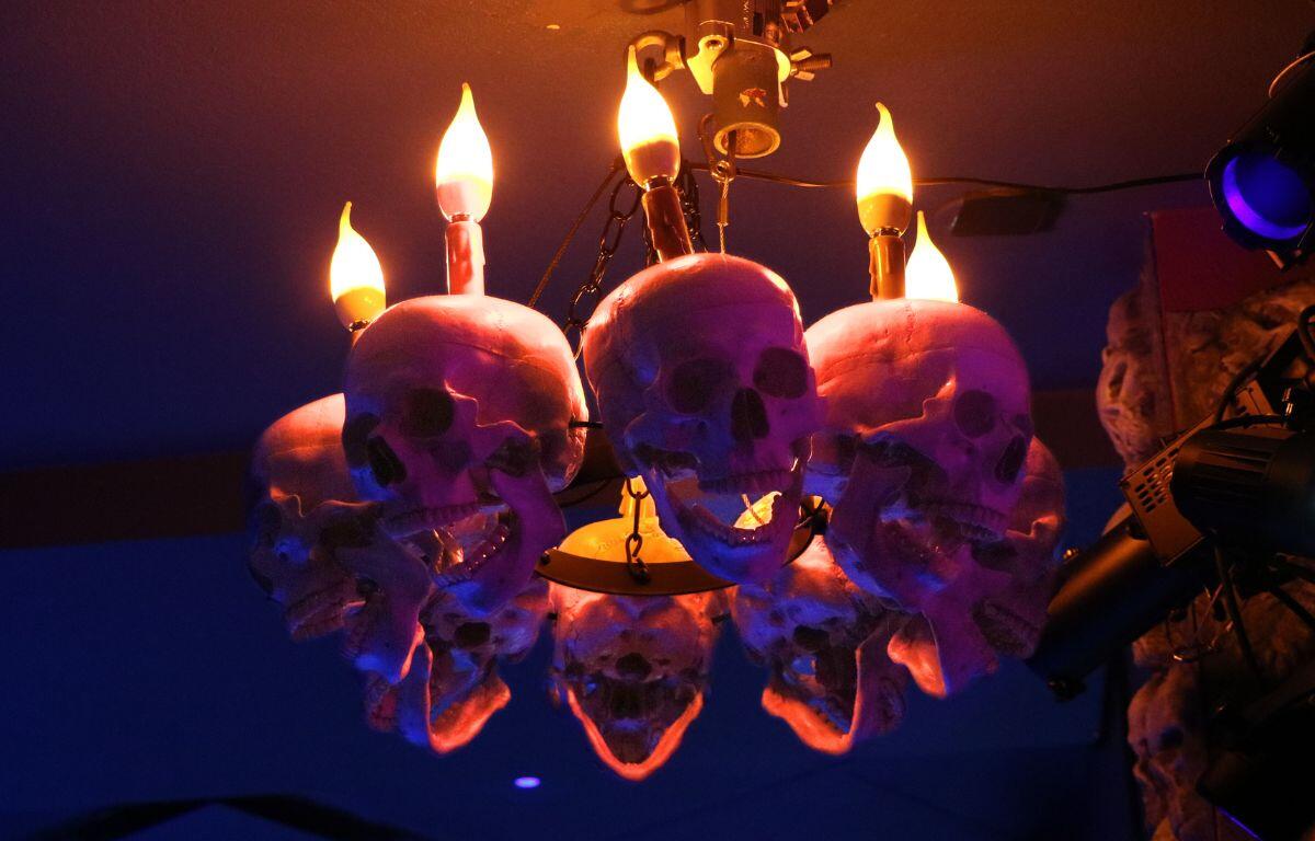 A lit chandelier decorated with skulls in a darkened room.