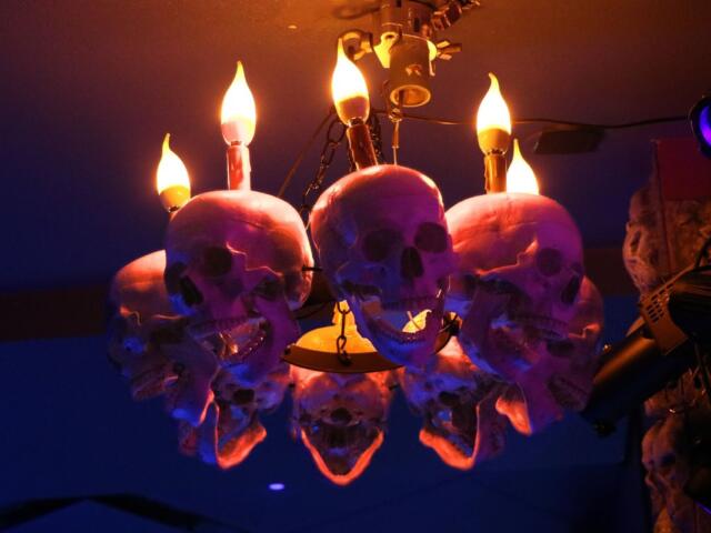 A lit chandelier decorated with skulls in a darkened room.
