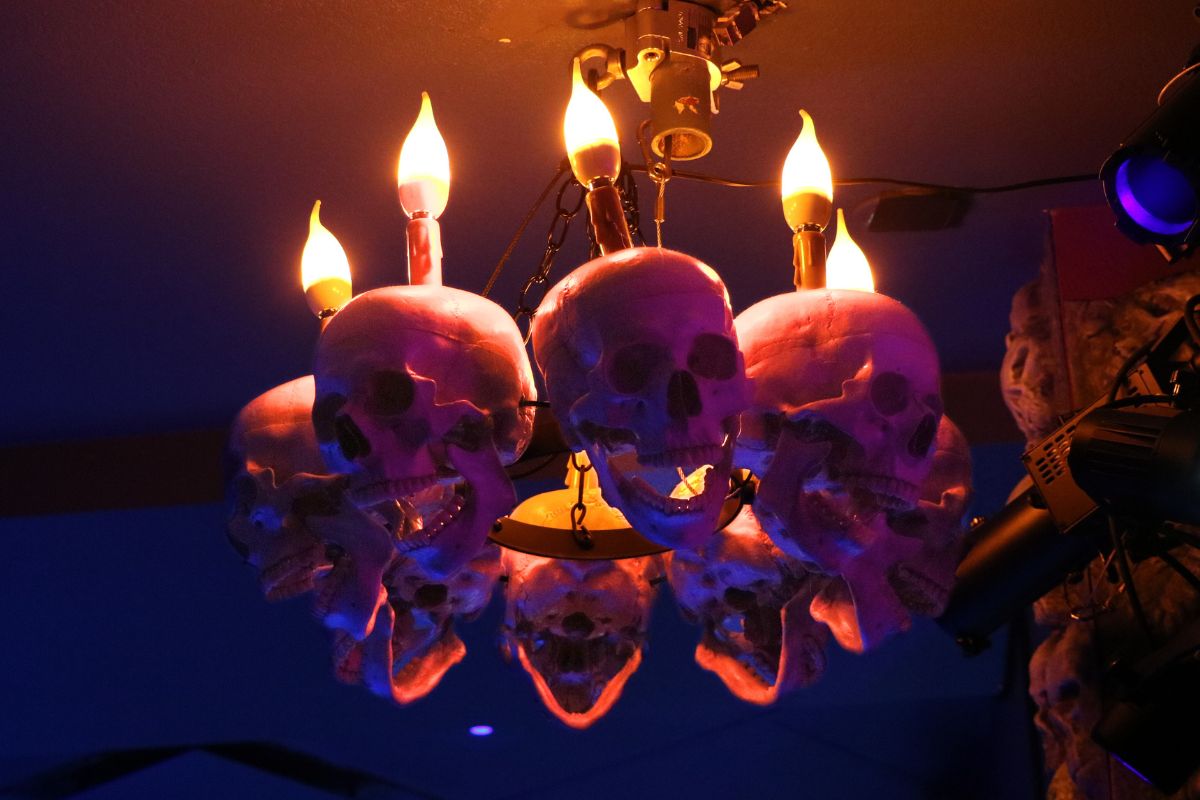 A lit chandelier decorated with skulls in a darkened room.