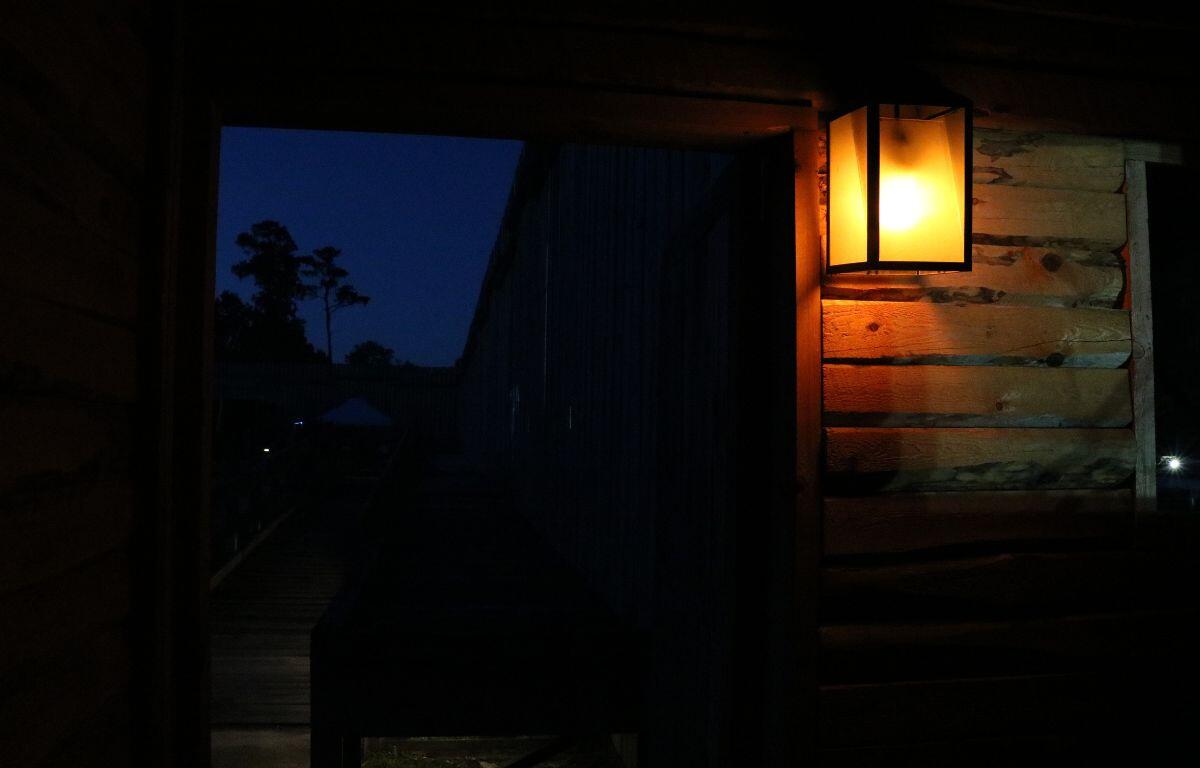 A wooden building has an open door that leads into a large field with walls surrounding it and a lantern lighting the room.