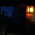 A wooden building has an open door that leads into a large field with walls surrounding it and a lantern lighting the room.