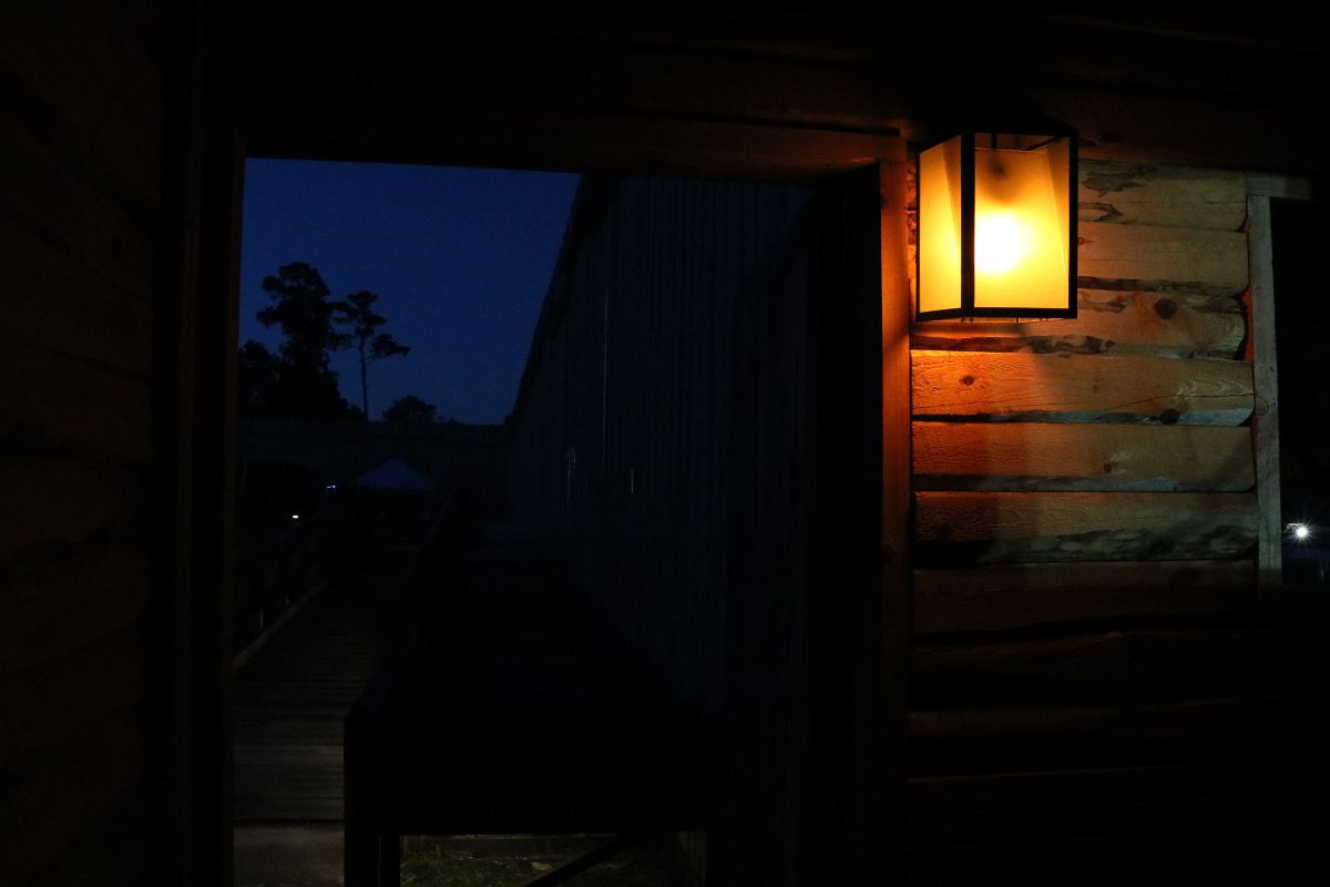 A wooden building has an open door that leads into a large field with walls surrounding it and a lantern lighting the room.