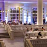 Guests seated at round tables in a spacious, well-lit hall with white decor and soft purple lighting.