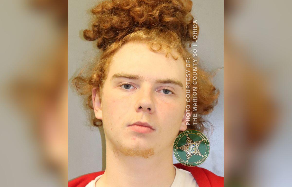 Red haired man, with his hair in a man bun, in a white and orange jump suit.