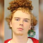 Red haired man, with his hair in a man bun, in a white and orange jump suit.