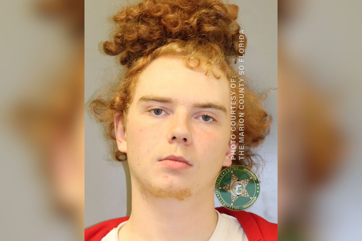 Red haired man, with his hair in a man bun, in a white and orange jump suit.