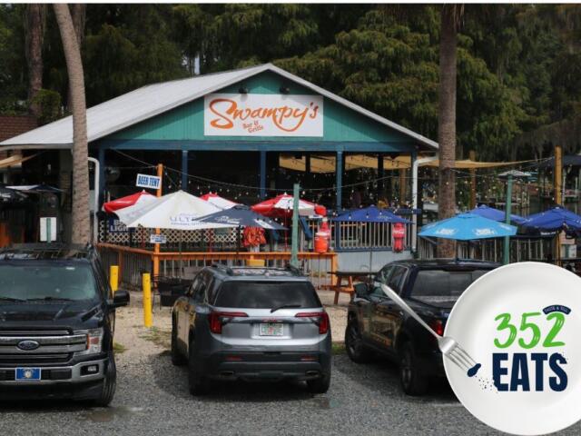 Exterior view of Swampy’s Bar & Grille with outdoor seating, colorful umbrellas, and parked vehicles in front.