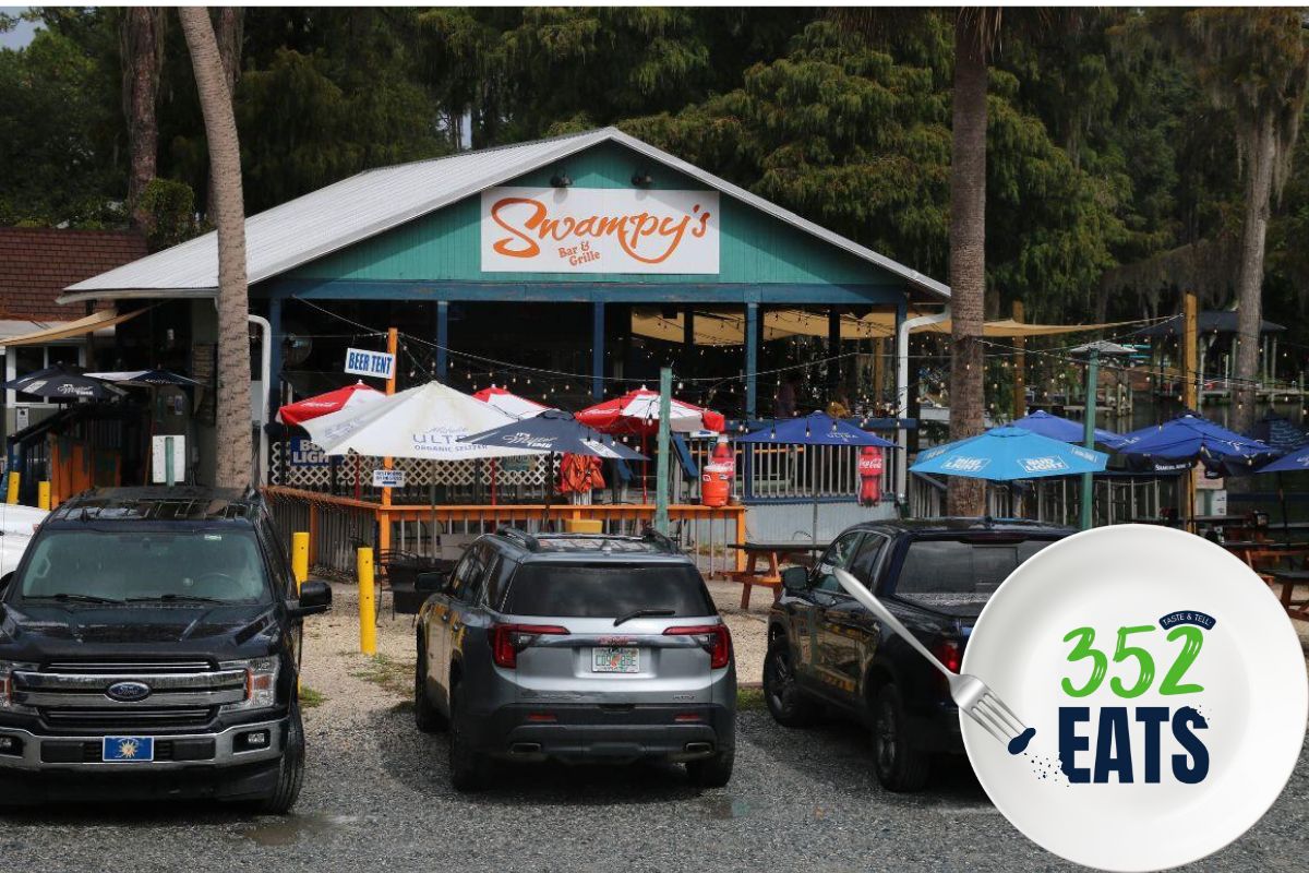 Exterior view of Swampy’s Bar & Grille with outdoor seating, colorful umbrellas, and parked vehicles in front.