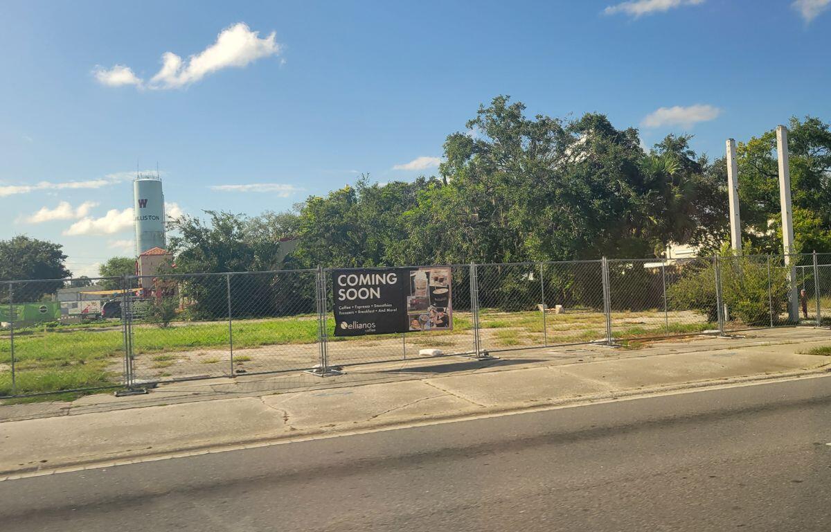 A vacant, cleared lot with a water tower for the town of Williston. It is a fenced area with a banner stating the upcoming Ellianos location.