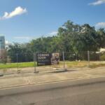 A vacant, cleared lot with a water tower for the town of Williston. It is a fenced area with a banner stating the upcoming Ellianos location.