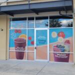 A tan colored building in a outdoor shopping plaza. Window clings are advertising a new Planet Smoothie.