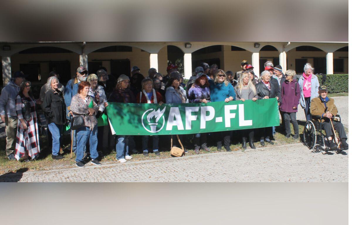 A group of people standing beside and behind an elongated banner, with a barn in the background.