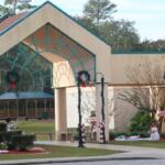 An open pavilion with lamp posts along a paved walkway leading toward it has Christmas decorations around it. The decorations include candy canes, wreaths snowman and deflated inflatable characters.
