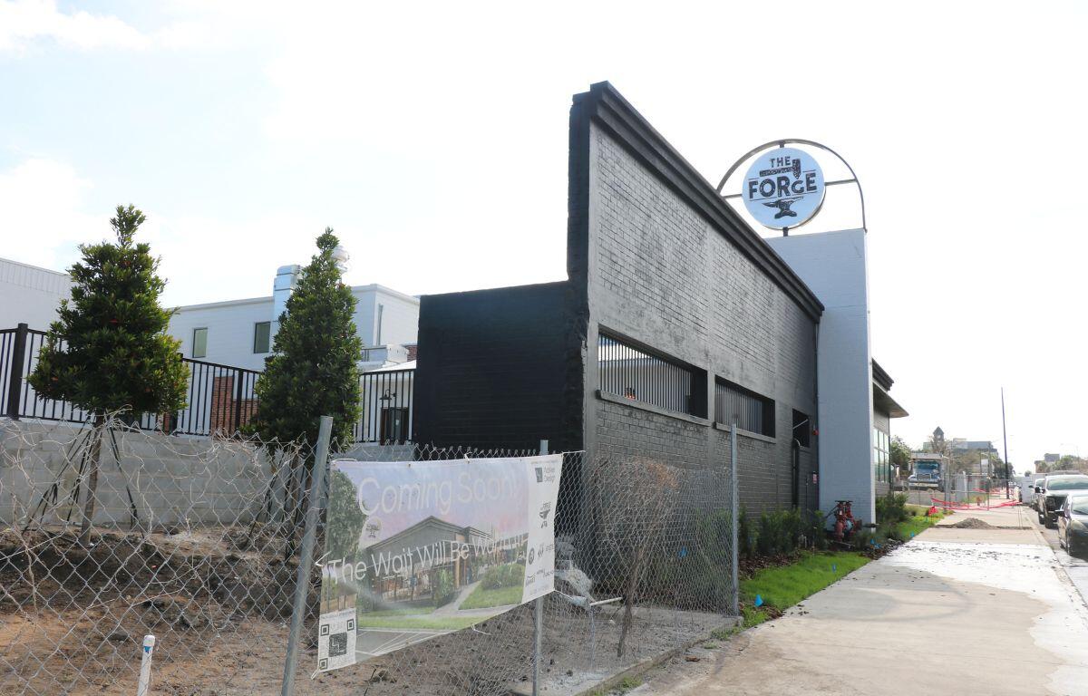 Street-level view of the exterior of a modern grey building under construction, surrounded by fencing.