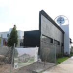 Street-level view of the exterior of a modern grey building under construction, surrounded by fencing.
