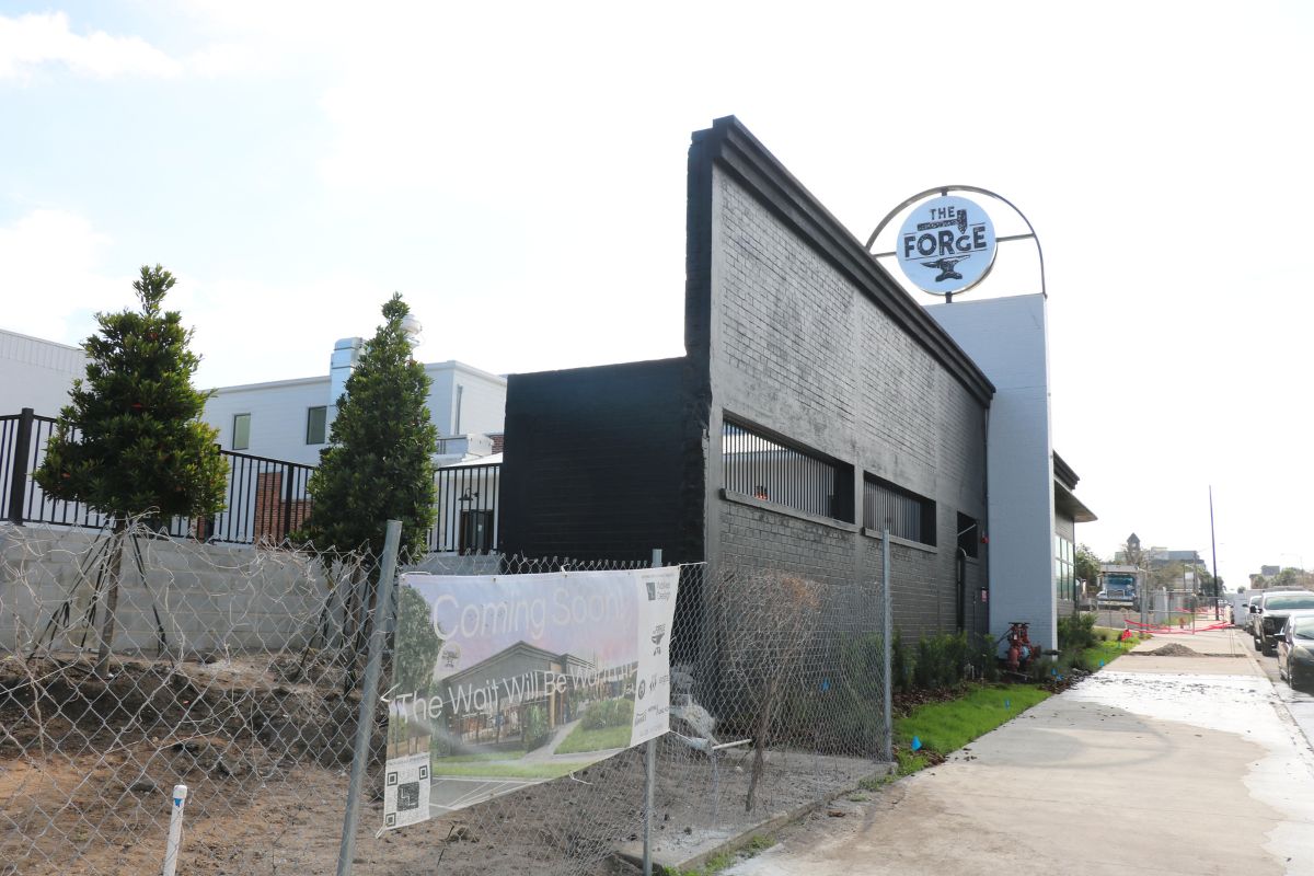 Street-level view of the exterior of a modern grey building under construction, surrounded by fencing.