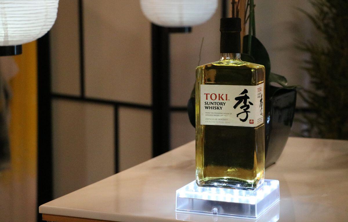 A green bottle of whiskey stands on a lit display in a Japanese style setting.