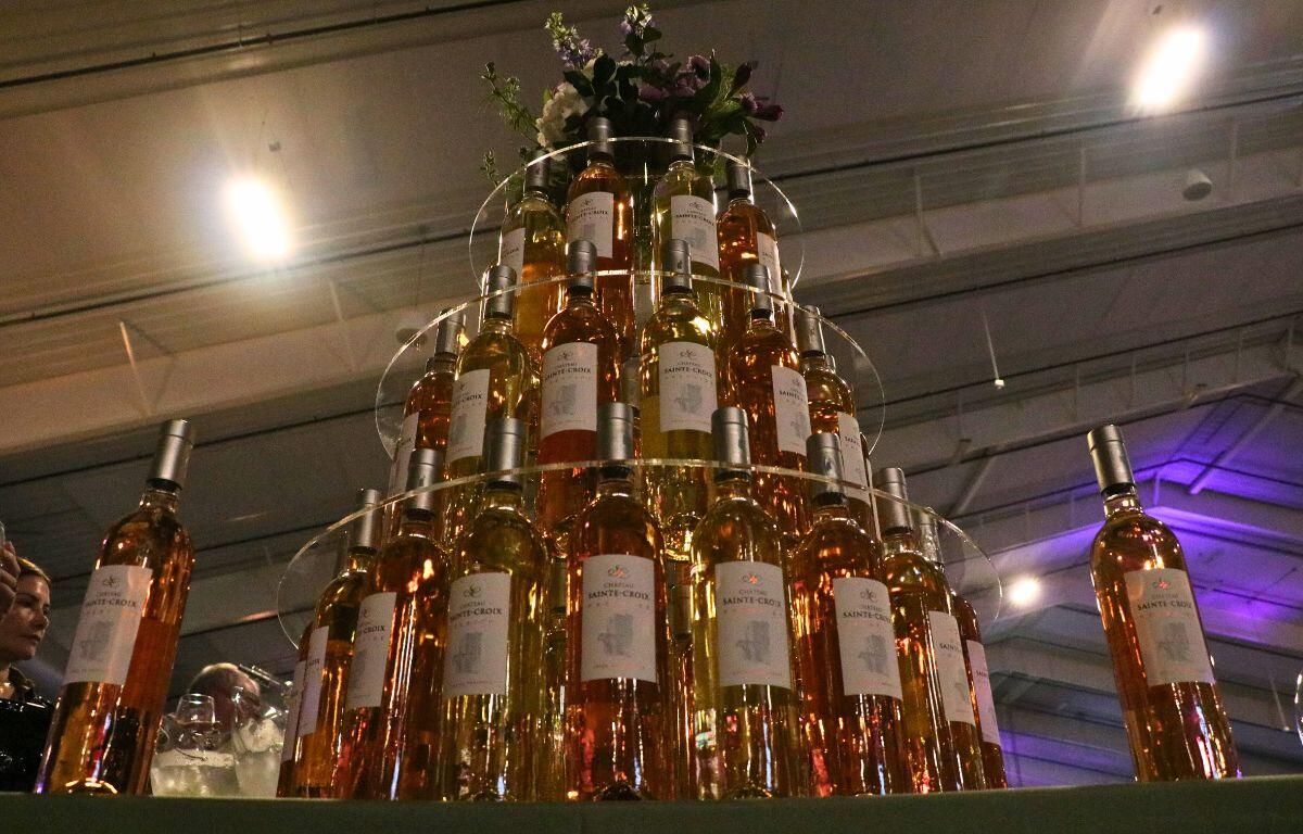 A tower of alcohol bottles has two bottles on either side of it and flowers on top. In the background is the ceiling of a venue.