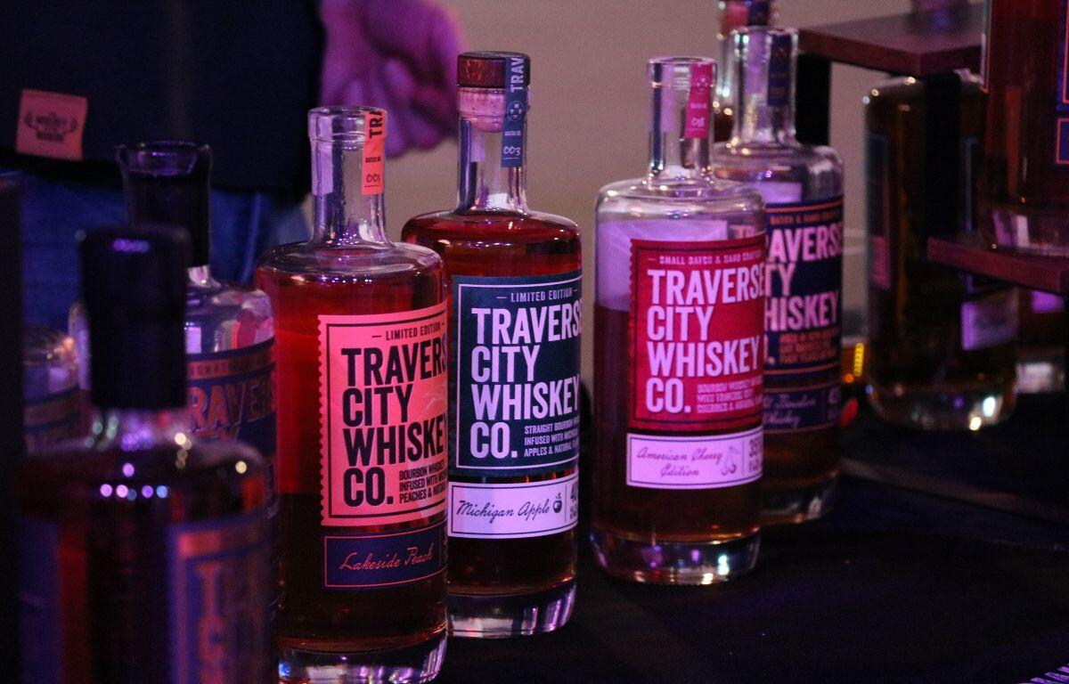 Multiple alcohol bottles are lined up on a table with a black tablecloth with labels reading, "Traverse City Whiskey Co."