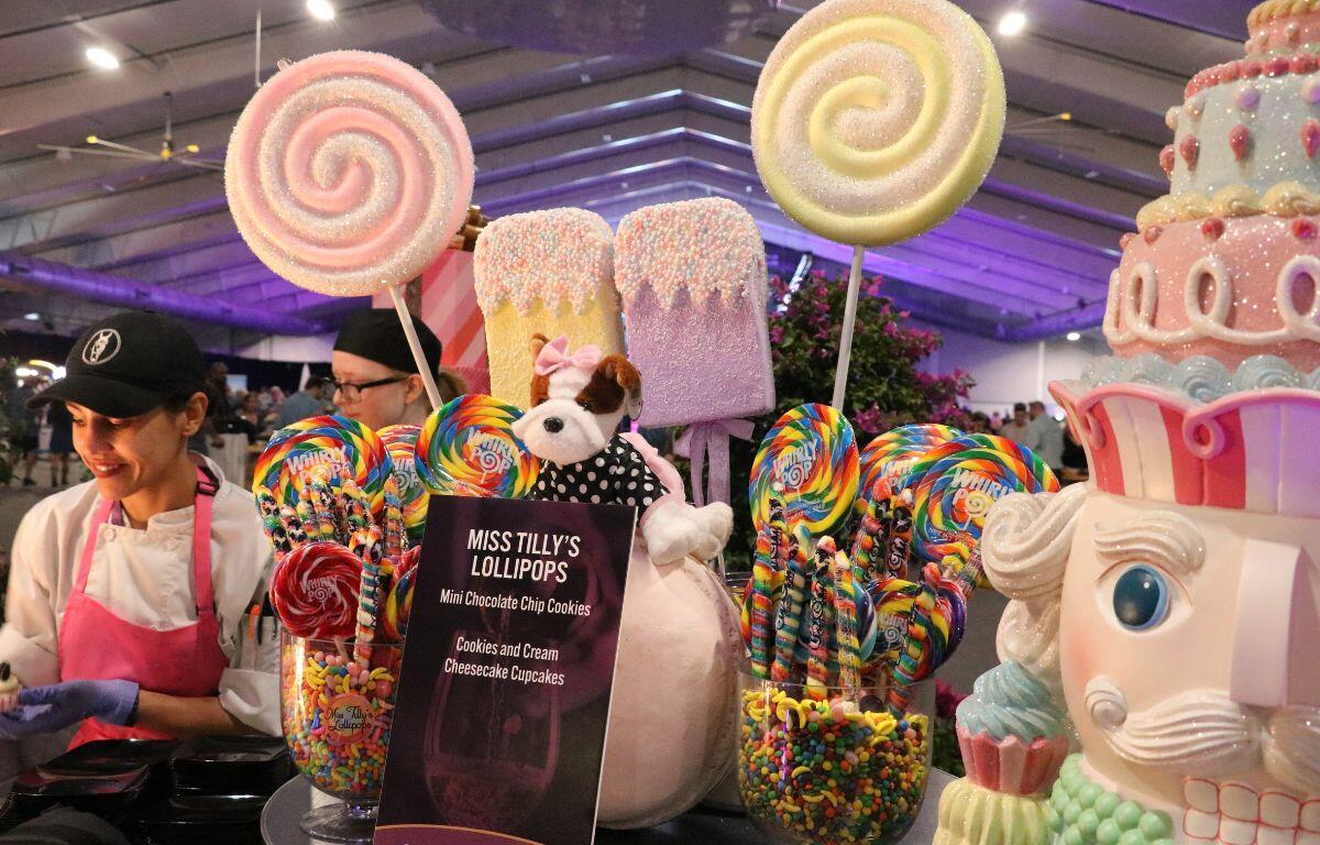 A table covered in lollipop, popsicle, a puppy doll and a large nutcracker displays features candys in cups and a sign reading, "Miss Tilly's Lollipops."