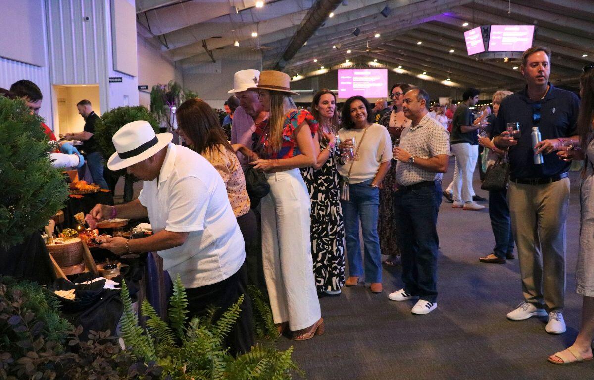 A group of people are lined up at a booth with decorative plants in the foreground.