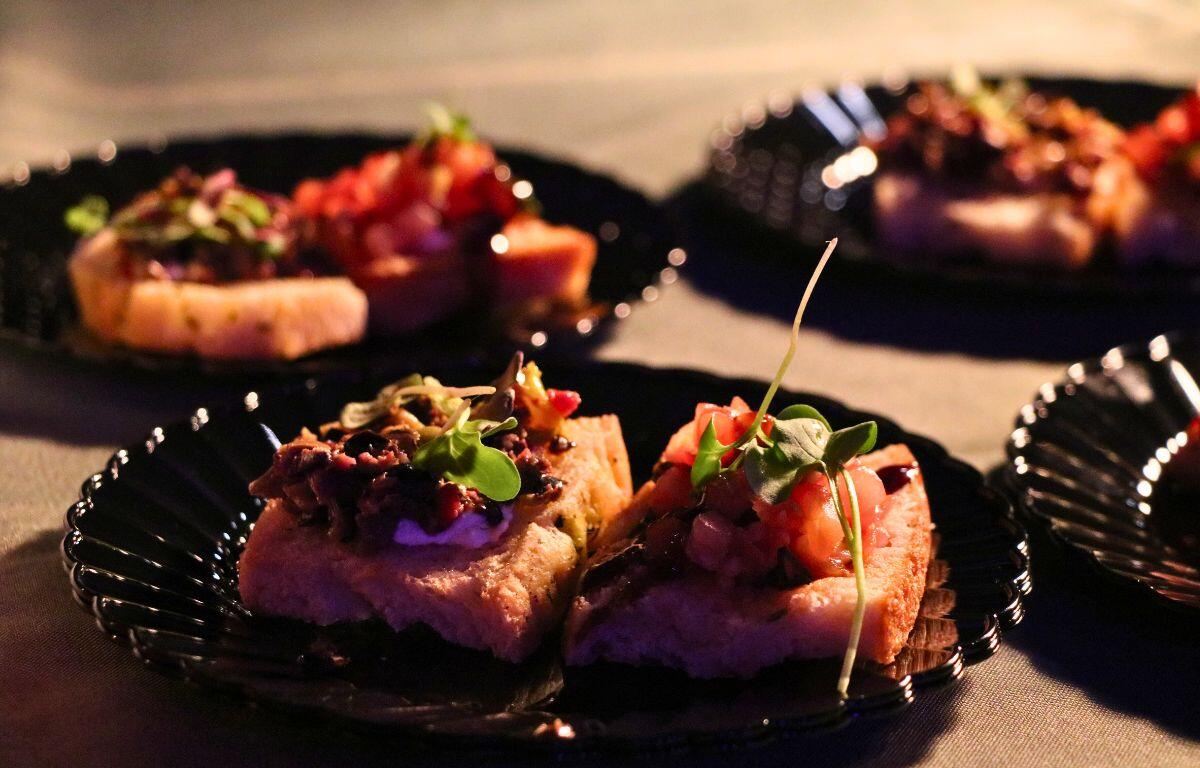 A dish covered in garnishes on a black plate under a warmer.
