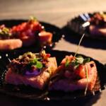 A dish covered in garnishes on a black plate under a warmer.