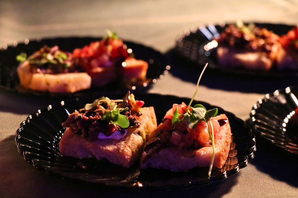 A dish covered in garnishes on a black plate under a warmer.